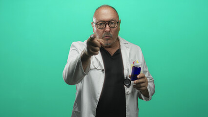 Man doctor in white coat holds blue bottle in right hand and points finger to label in studio;...