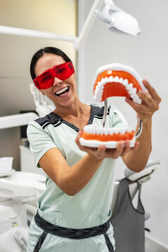 Friendly dentist explaining oral care using oversized mouth model