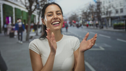 Woman smiling and clapping on a busy city street, showcasing outdoor urban ambiance with diverse...