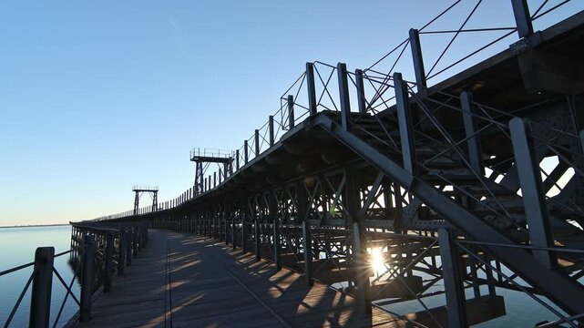 Dramatic low-angle view of Muelle del Rio Tinto structure, Huelva, Spain. Industrial heritage, engineering framework, and sun starburst.