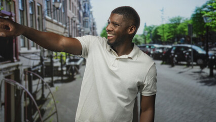 Man wearing white polo points arm with visible hand toward street, looking to side near parked cars...