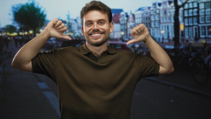 Naklejka premium Man with thumbs pointing to chest on city street with canal houses and parked bikes nearby; confidence.