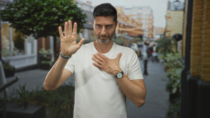 Man raising right hand and placing left hand on chest on street with blurred pedestrians and...