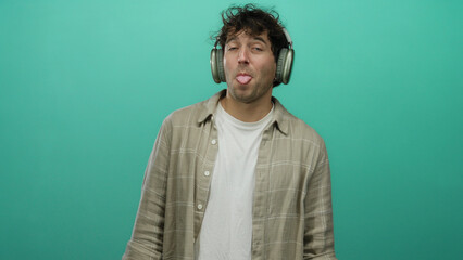Fototapeta premium Man enjoying music with headphones, eyes closed, wearing casual shirt against green background, expressing joy and relaxation.