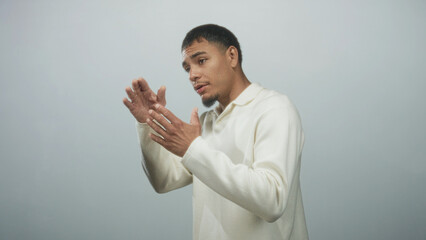 Man gesturing with open hands while speaking in a plain studio, wearing a cream sweater and facing left; thoughtful explanation.