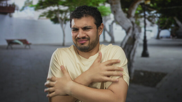 Man grimaces showing face on a city street during daytime with a bench, tree, and lamppost behind him; disgust.