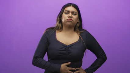 Obraz premium Woman clutching stomach and wincing with hand on abdomen in a studio against a purple backdrop; discomfort nausea concern.