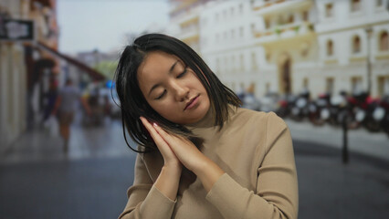 Young woman gesturing sleep on busy city street in daylight with buildings and people blurred in background capturing urban life vibe
