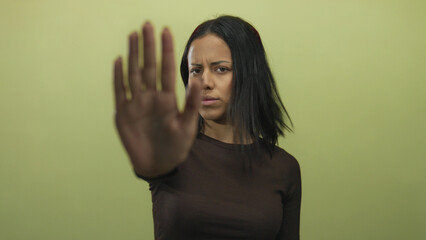 Woman gesturing stop with her hand against a yellow background, expressing firmness and seriousness in an isolated setting, emphasizing a message of rejection and boundary.