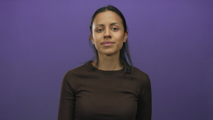 Fototapeta premium Woman smiling against isolated purple background, extending hand forward, wearing dark shirt, young hispanic female posing confidently, studio portrait for stock image.