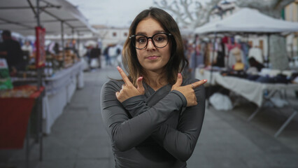 Woman wearing glasses arms crossed pointing fingers outward in street market stalls and souvenir...