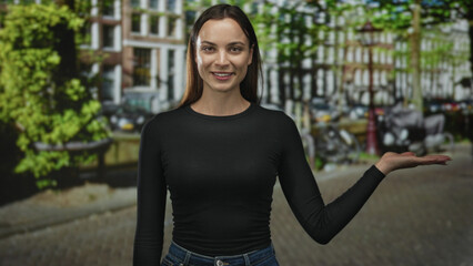 Woman holding palm up presenting gesture on a city street with canal houses and bicycles in soft focus; friendly welcome.