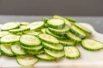A low stack of cucumber slices spreads across a cutting board. The shallow depth of field emphasizes their vibrant green edges and juicy interiors.