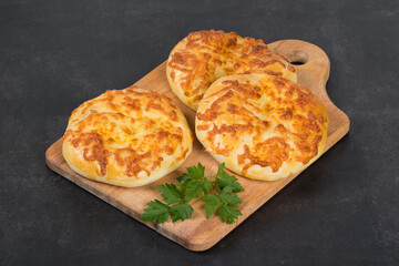 Small Round Cheese pie. Flatbread with cheese. With parsley. On a wooden board. Dark background. Close up