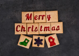 Christmas square cookies with colored marmalade filling in the shape of the words Merry Christmas and Christmas sock, snowflake, mitten. Dark background. Top view