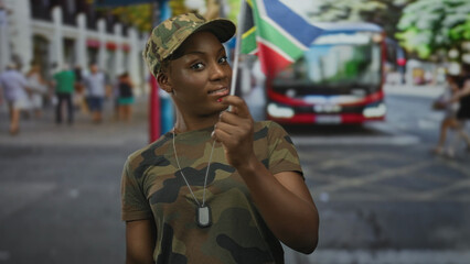 Fototapeta premium Woman soldier wearing camouflage uniform and dog tag necklace waves south african flag on street; pride duty.