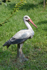 Obraz premium A weathered, white and black garden sculpture of a stork stands on a patch of green grass in bright sunlight