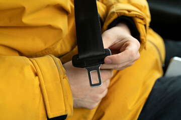 A person wearing a yellow jacket secures their seat belt inside a vehicle