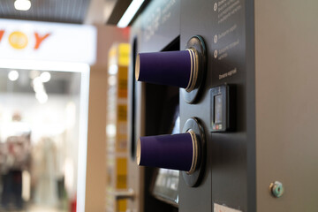 Two coffee cups are positioned at a self-serve coffee machine in a mall