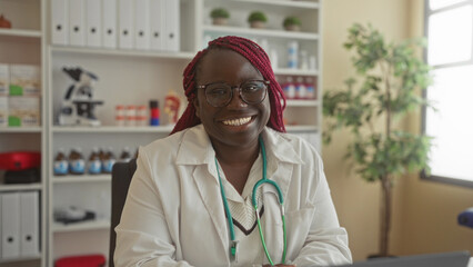Woman doctor smiling in a clinic with stethoscope and glasses, surrounded by medical equipment,...