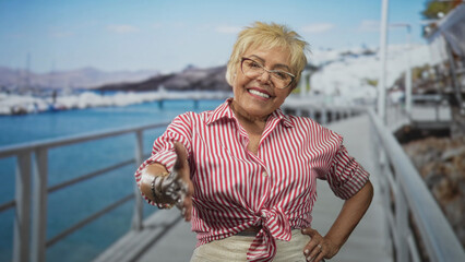 Fototapeta premium Woman extends right hand for handshake with bracelets and glasses on a street pier by the marina, smiling and offering greeting to camera; warm welcome.