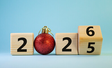 2026 New Year symbol. Businessman turns wooden cube and changes Year 2025 to 2026. Beautiful light blue background with Christmas ball. Copy space. Business and 2026 happy new year concept
