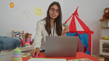 Young hispanic woman teacher holds colored number shapes during a video call in building; learning engagement.