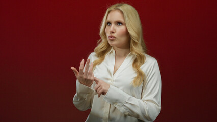Woman counting on fingers with thoughtful expression against red background, wearing a white shirt,...