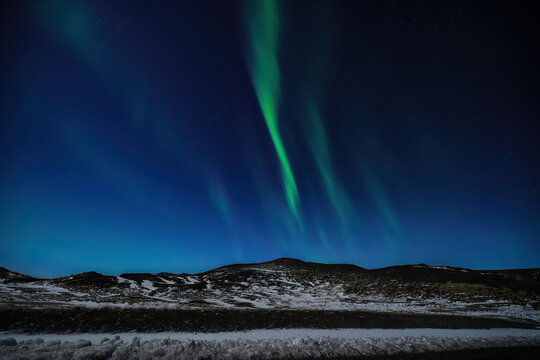 View of the ethereal green northern lights dance across the indigo sky over the snow-dusted landscape, creating a magical scene, Vatnsskard valle, Hunabygga, Iceland.
