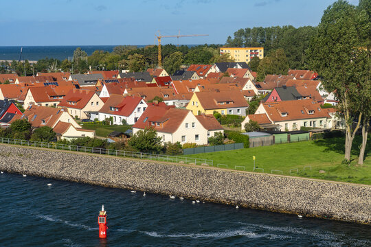 View of red-roofed houses clustered along the water's edge, separated by a sturdy stone wall, with the sea visible in the distance, Rostock, Rostock, Germany.