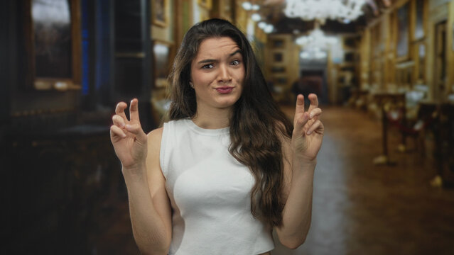 Woman making air quotes gesture with fingers in grand museum building hall lined with paintings; sarcasm irony skepticism mockery.