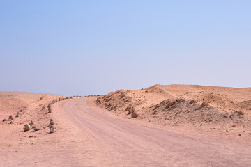 Dusty road winding through arid landscape under clear blue sky