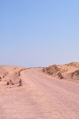 Dusty road winding through arid landscape under clear blue sky