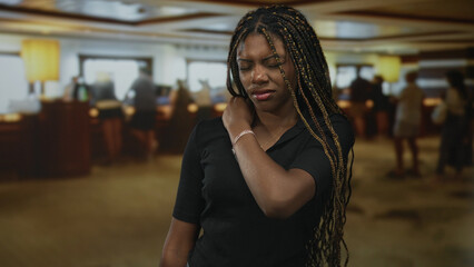 Woman with hand on neck in hotel lobby near checkin desk, closed eyes and slight grimace; discomfort travel.