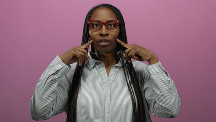 Obraz premium Woman with glasses gestures playfully against a vivid pink wall wearing a striped shirt focusing on self expression and personal style.