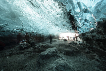 View of ethereal blue light filtering through the icy cavern as explorers venture into the depths, a chilling yet beautiful landscape, Vatnajokull, Southern Iceland, Iceland.
