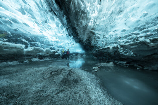 View of a cavernous ice cave with shimmering turquoise walls reflecting in the glacial pool below, Vatnajokull, Southern Iceland, Iceland.