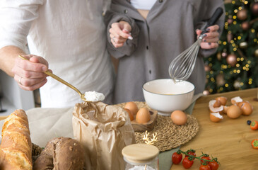 Man holding spoon with flour while woman uses whisk to mix ingredients in a bowl for Christmas baking. Holiday cooking at home.