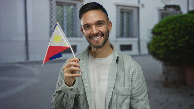Young man smiling holding philippine flag outdoors in urban street setting showcasing national pride and cultural identity in city environment.