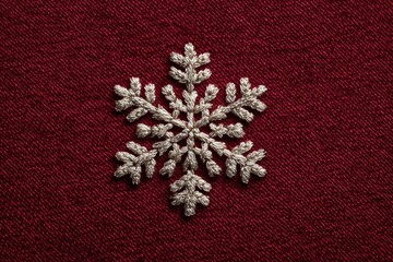 A snowflake embroidered on dark red fabric.