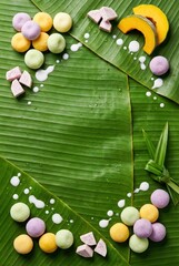 Thai dessert Bua Loi ingredients flat lay with colorful glutinous rice balls, pumpkin, taro and pandan leaves on banana leaf background with coconut milk drops and copy space for vertical menu design.