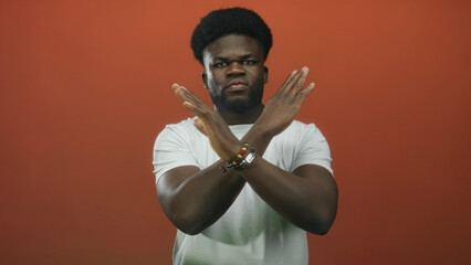 Man with arms crossed x showing hands and beaded necklace against orange wall in studio; defiance...