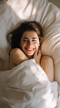 Smiling woman resting in bed surrounded by white sheets during morning light in cozy room