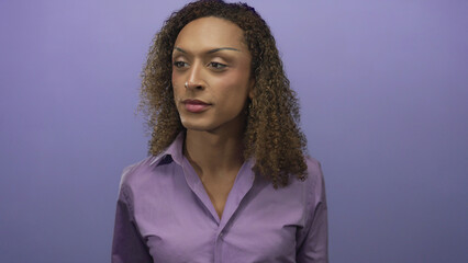 Transgender woman with curly hair and hoop earrings wearing purple shirt looks at camera in purple studio  confidence. © Krakenimages.com
