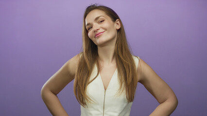 Fototapeta premium Young woman in white dress smiling with subtle smirk and hands on hips in purple studio session; self confidence empowerment pride.