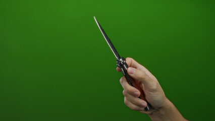 Man holding knife with isolated green background, highlighting the sharp metal blade in a gripping caucasian hand.