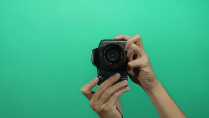 Man holding camera against green wall background showcases a close-up of hands handling...