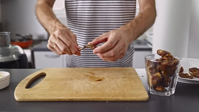 A person is carefully pitting fresh dates on a wooden cutting board in a clean, modern kitchen.