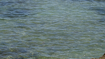 Clear turquoise water gently rippling under sunny skies in a tranquil mediterranean sea setting outdoors during a bright day.