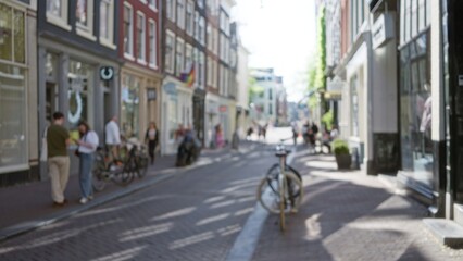Blurred scene of a european city street with people walking and cycling through the quaint town, showcasing bokeh and defocused elements in an urban outdoor setting.